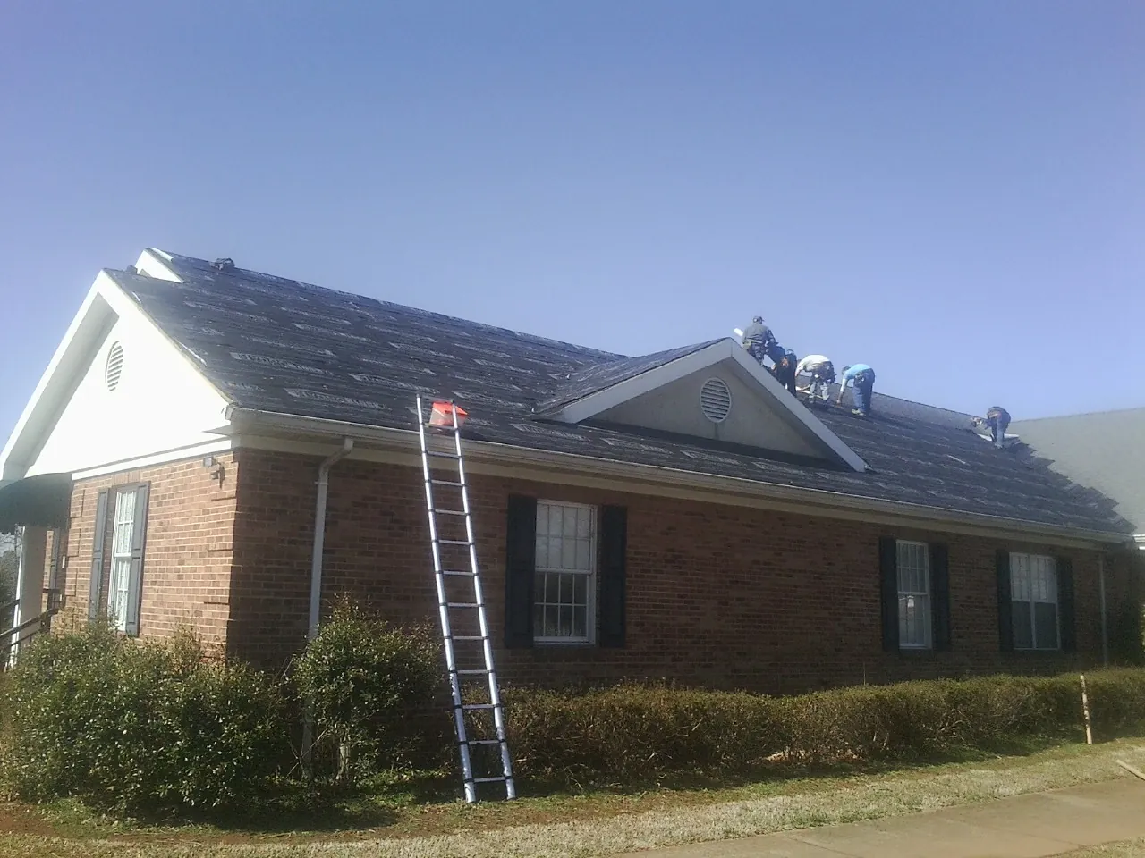 Crew tearing shingles off a brick ranch roof with a ladder set — Metal Roof Repair work by our crew in Dutch Flat