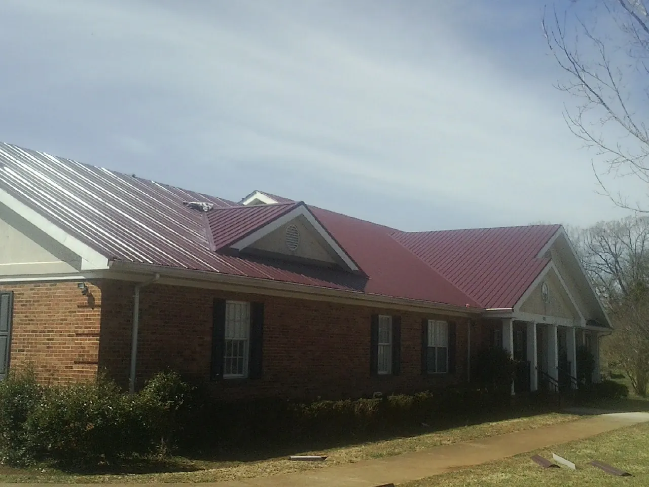Red metal roof with gabled entries on a long brick building, from a Hail Damage Roof Repair job in Dutch Flat