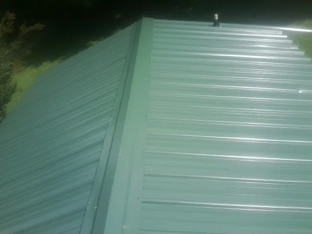 New green metal panels meeting at the ridge of a roof — Flat Roof Repair work by our crew in Dutch Flat