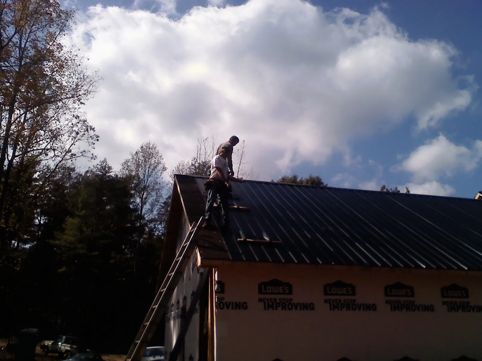 Roofer fastening dark metal panels high against a cloudy sky, from a Roof Inspection job in Dutch Flat