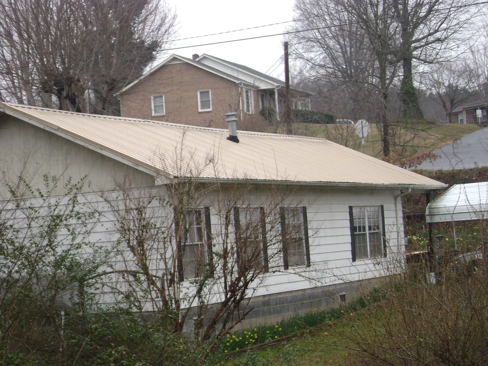 Tan metal roof on a white sided house set into a hillside — Commercial Roofing by Roofing Brothers in Dutch Flat